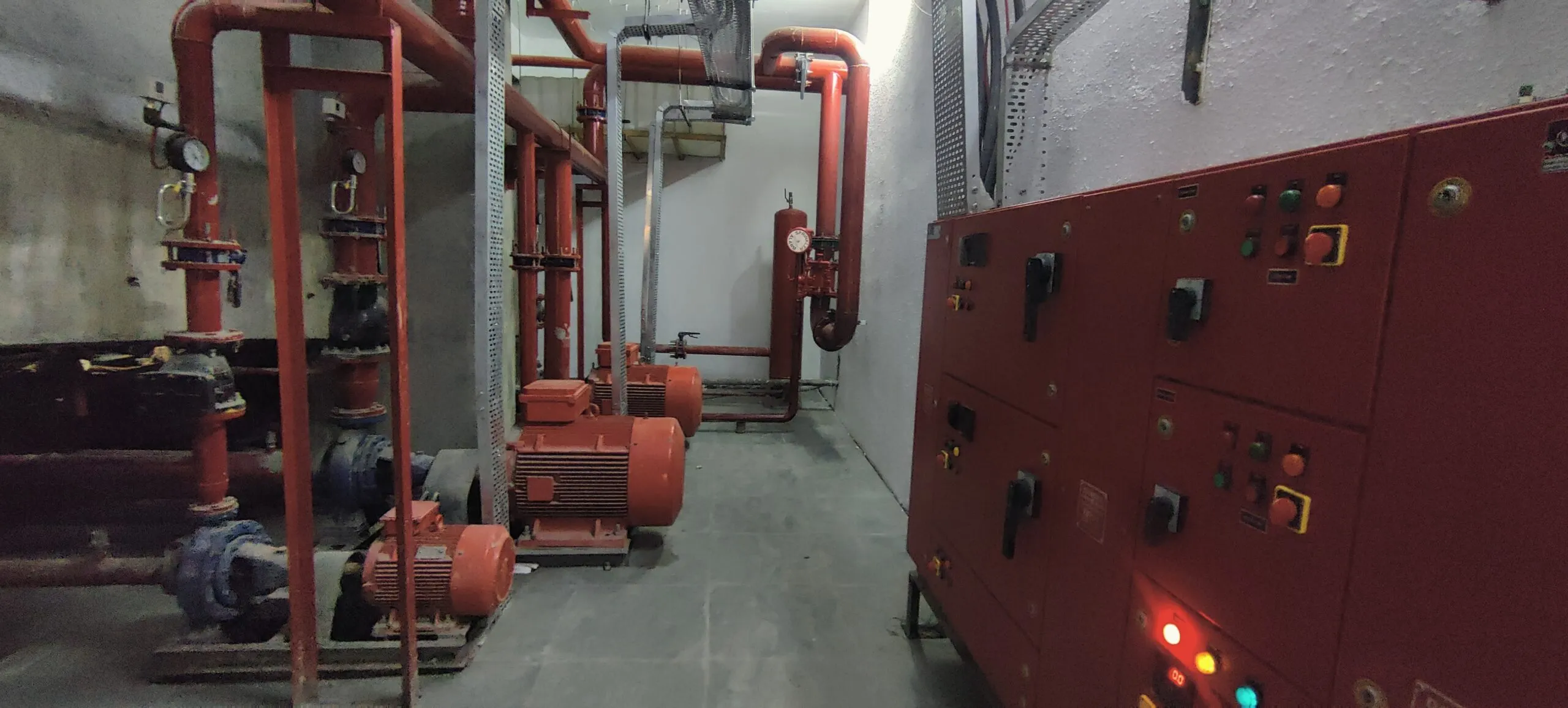 Fire pump room with red pumps, pipework and a fire pump control panel